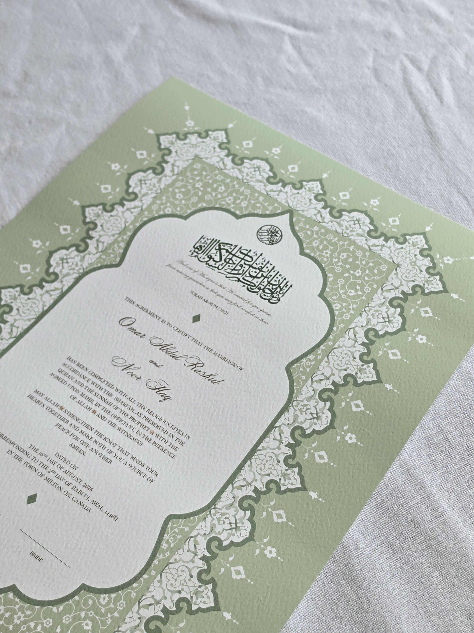 A green and white nikah certificate featuring elegant Arabic calligraphy and intricate lace-like border patterns, laid flat on a textured white fabric background.